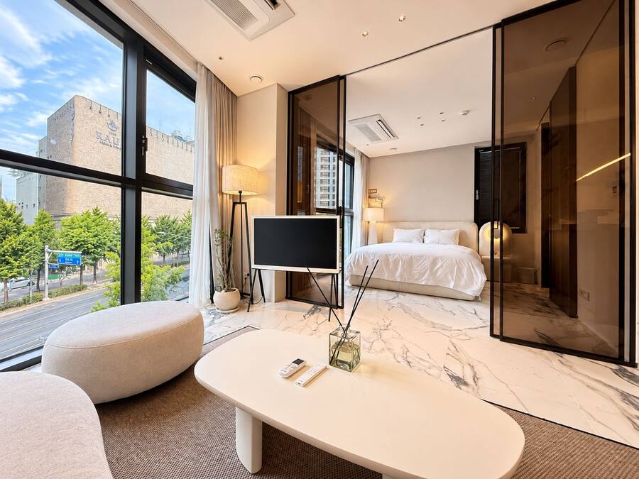Habitación de hotel moderna con una cama grande, un televisor de pantalla plana, una zona de estar con una mesa y vistas a la ciudad.