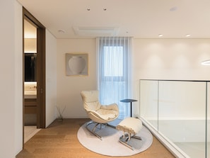A modern living room with a round rug, a cushioned stool, a chair, a floor lamp, and a large window with sheer curtains. - Caelum Black Gangnam Luxury Residence (Seoul)