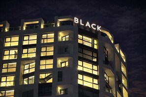 Ein mehrstöckiges Gebäude mit beleuchteten Fenstern und dem großflächig angebrachten Schriftzug 'BLACK' an der Fassade.