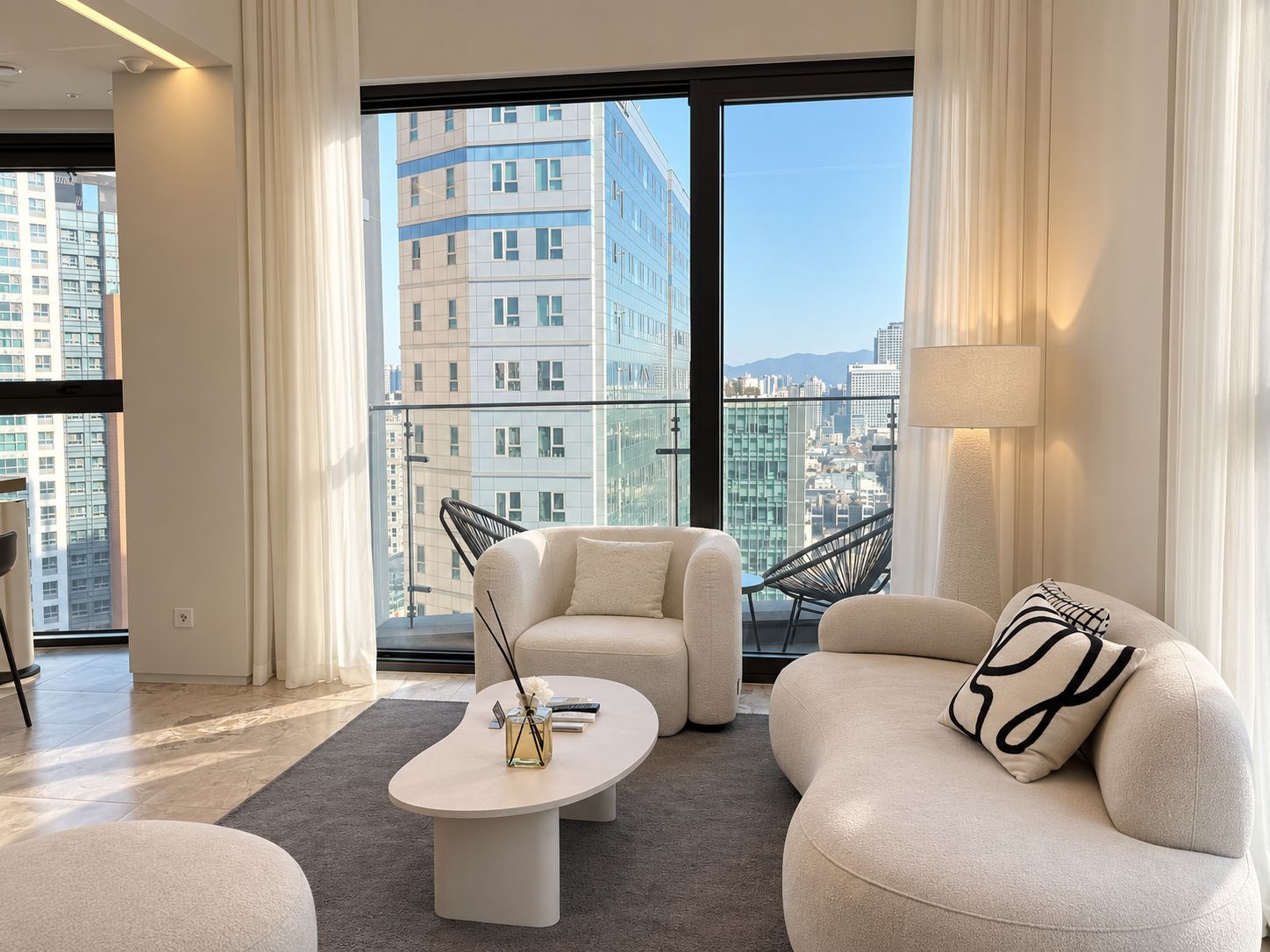 Un salon moderne comprenant un canapé, un fauteuil et une table basse, et offrant une vue sur la ville grâce à de grandes fenêtres.