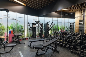 Een sportschool met diverse fitnessapparaten, grote ramen en uitzicht op groen.