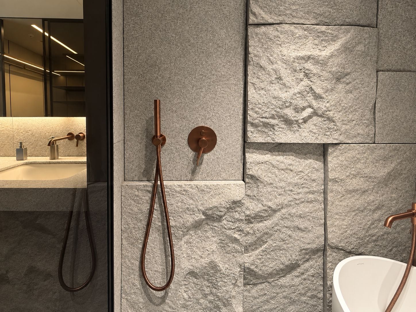 Een moderne badkamer met een wand met een steenstructuur, een wastafel met een kraan en een douche met een handdouche.
