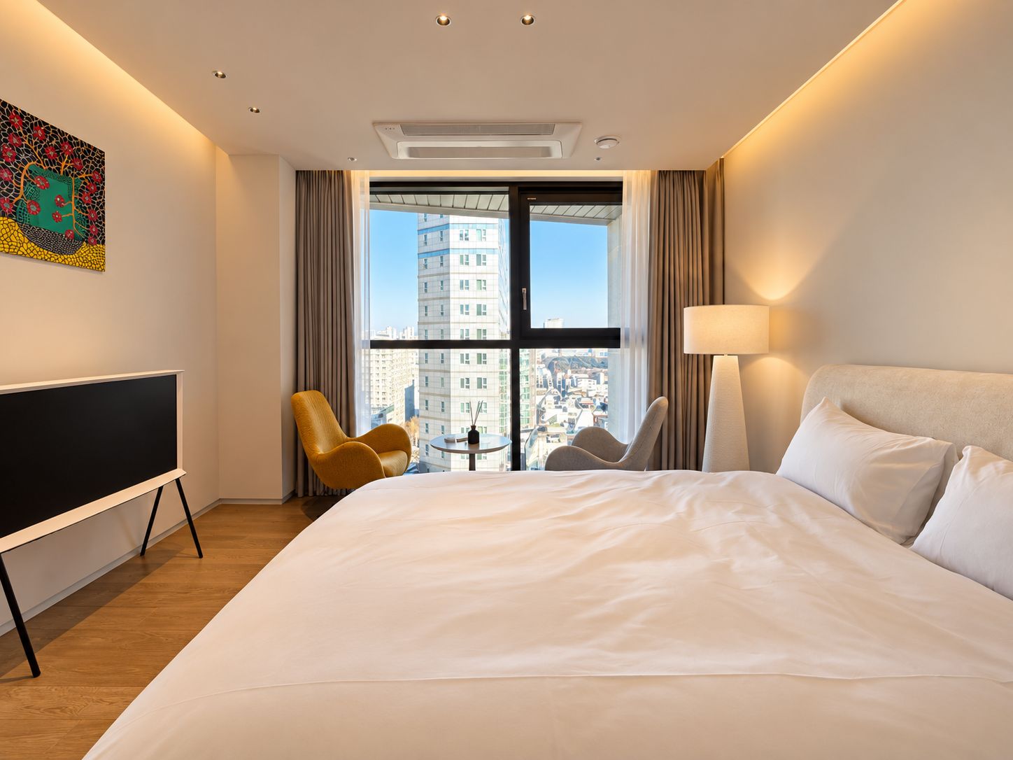 Habitación de hotel con una cama grande, televisión de pantalla plana, escritorio y vistas a la ciudad a través de un ventanal.