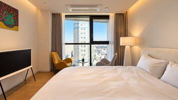 Habitación de hotel con una cama grande, televisión de pantalla plana, escritorio y vistas a la ciudad a través de un ventanal.