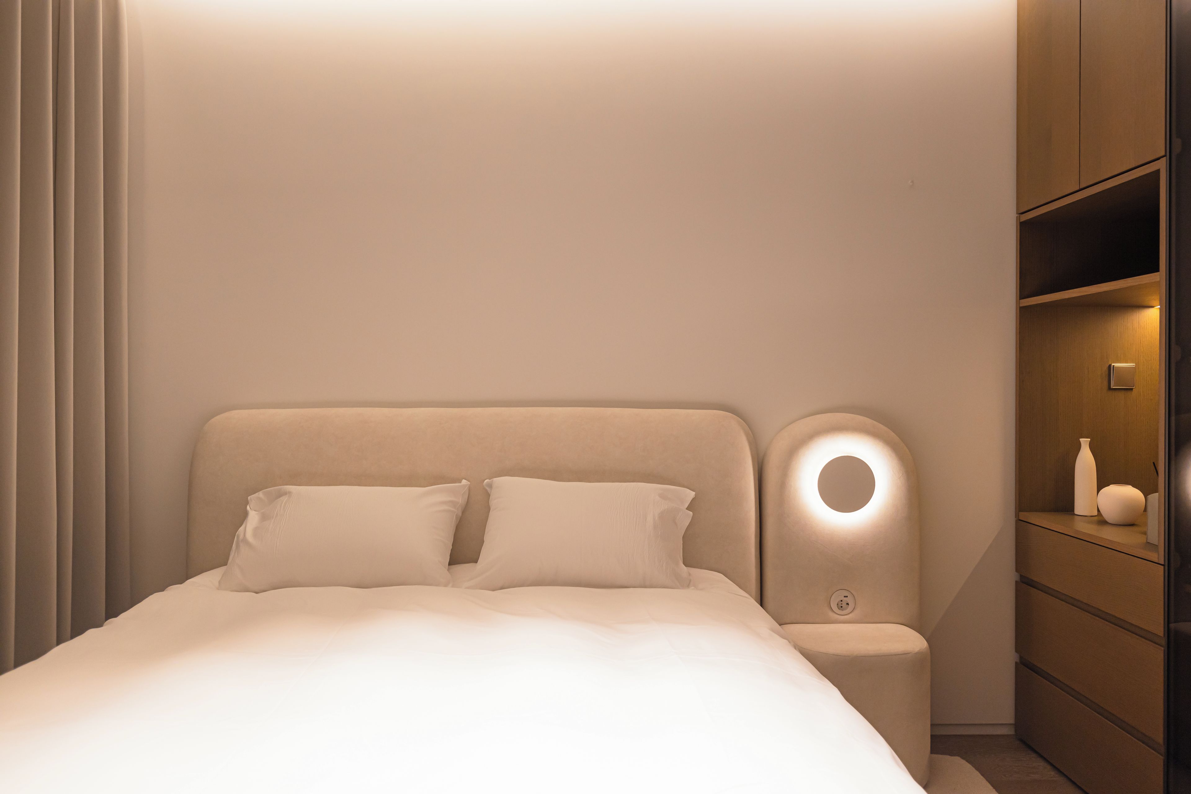 A modern bedroom with a bed, bedside table, and a nightstand with a lamp.