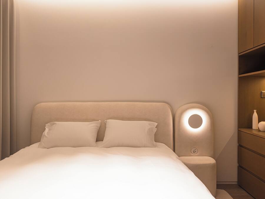 A modern bedroom with a bed, bedside table, and a nightstand with a lamp.