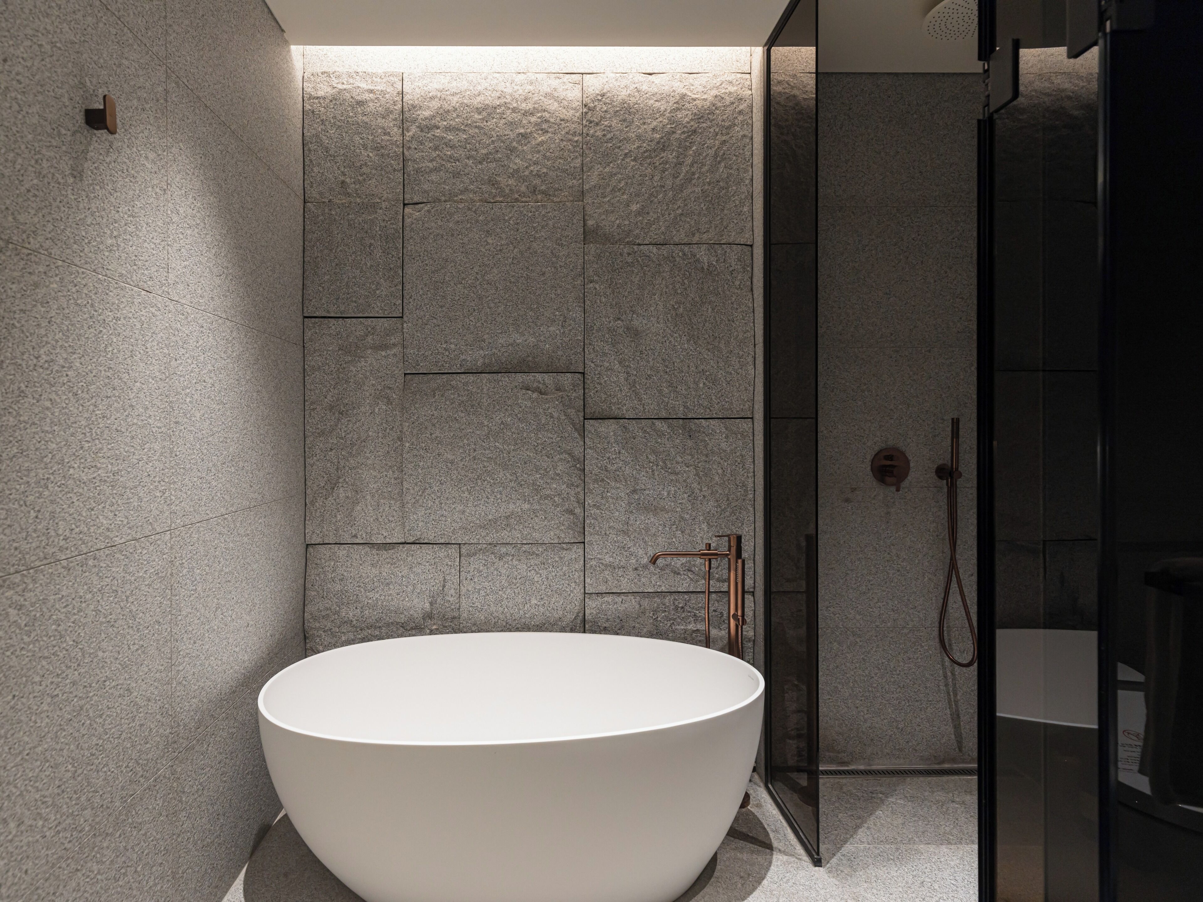 Un baño moderno con una bañera independiente, una cabina de ducha con paredes de vidrio y una pared con textura de piedra.