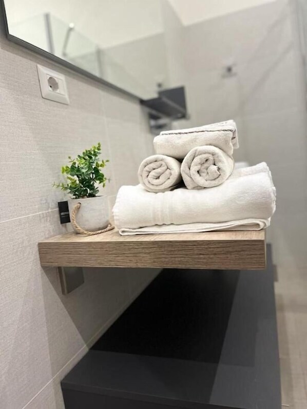 A bathroom with a wooden shelf holding rolled towels and a small potted plant. - La piazzetta Anzio (Anzio)