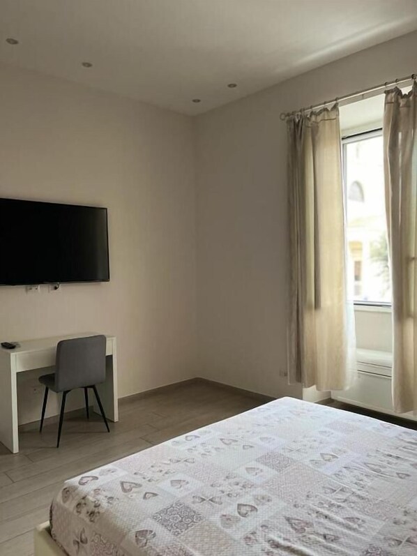 A bedroom with a bed, a desk, a chair, a TV, and a window with curtains. - La piazzetta Anzio (Anzio)