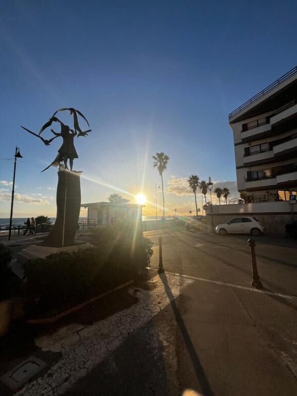 A statue of a figure with wings, a building, and a sunset in the background. - La piazzetta Anzio (Anzio)