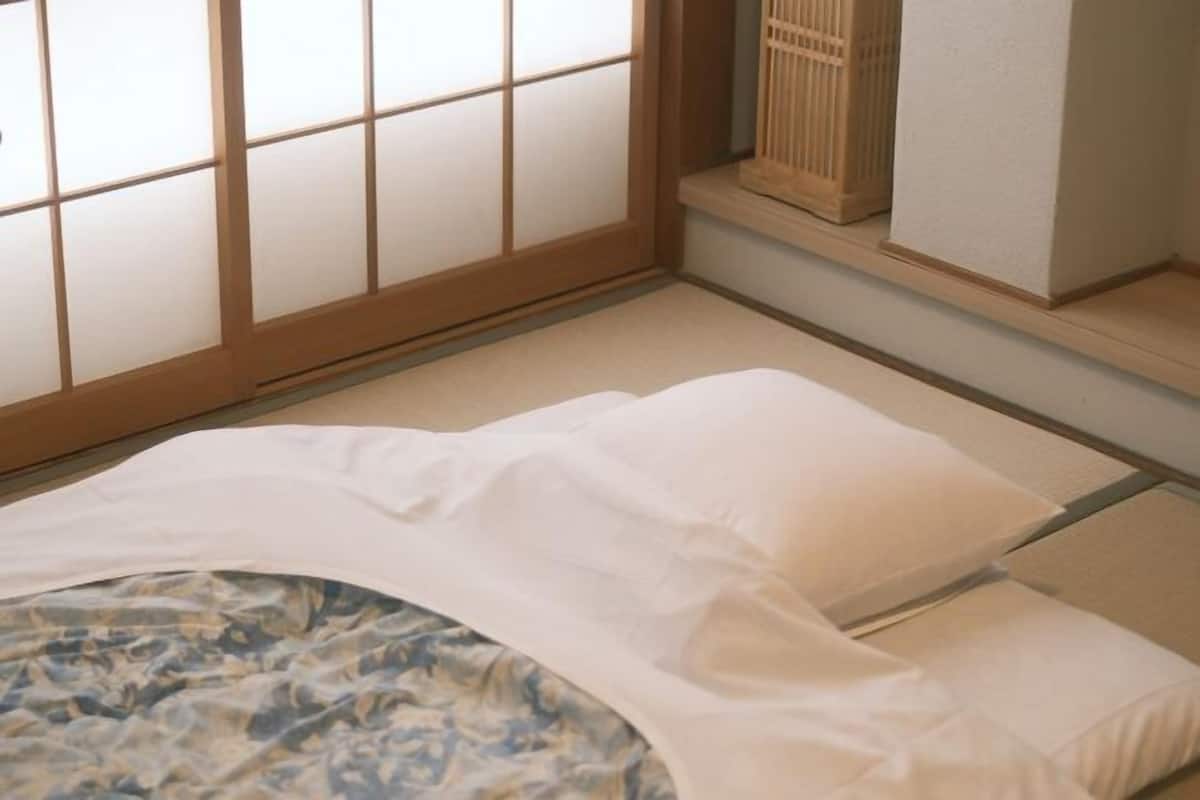 Una habitación japonesa tradicional con suelo de tatami, una cama baja con ropa de cama blanca y una puerta corredera shoji.