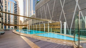 An indoor swimming pool with a wooden deck, surrounded by high-rise buildings. - DAMAC Maison Mall Residences - Downtown (Dubai)