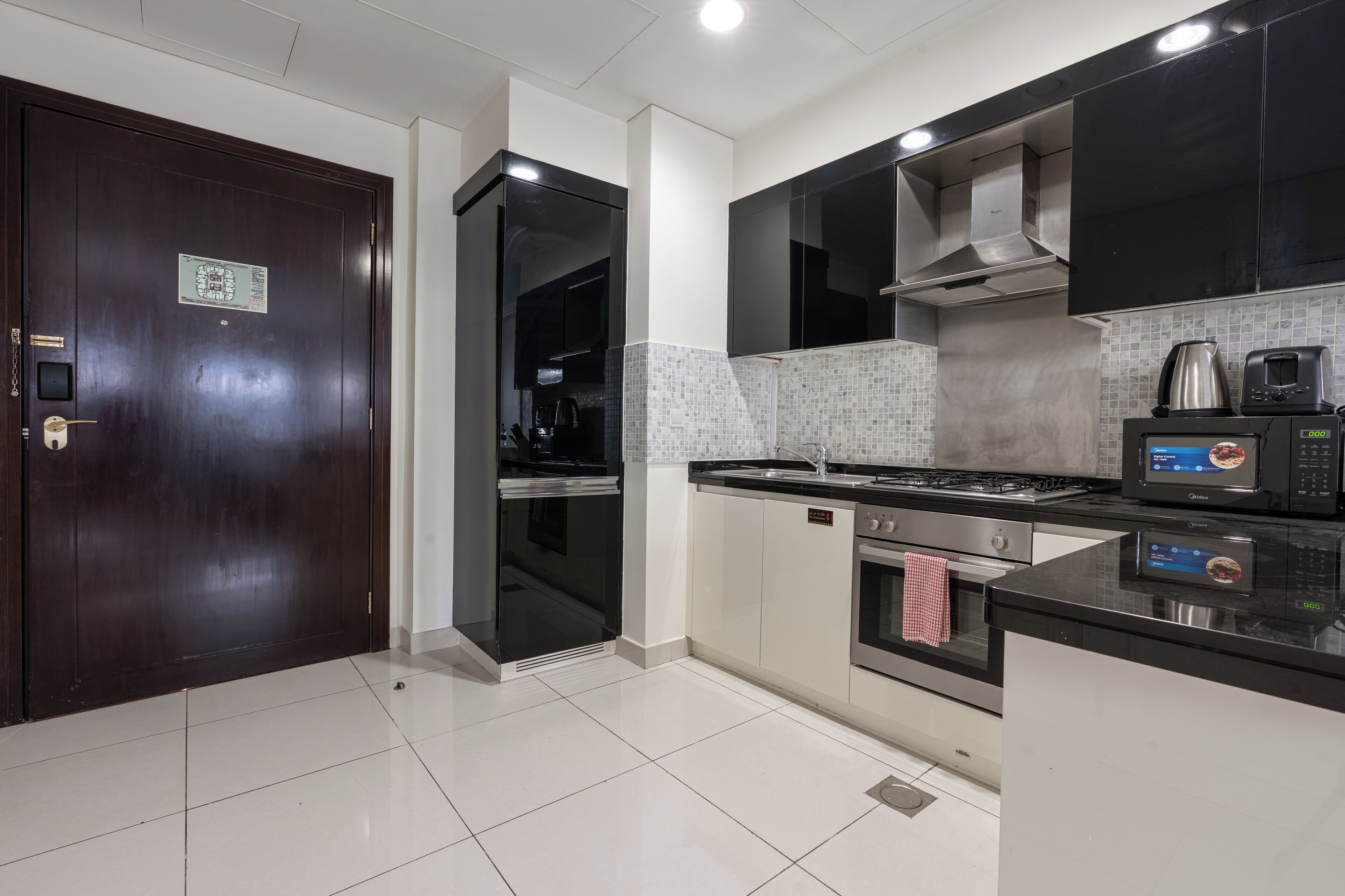 A modern kitchen with a dark wooden door, stainless steel appliances, and a tiled backsplash.