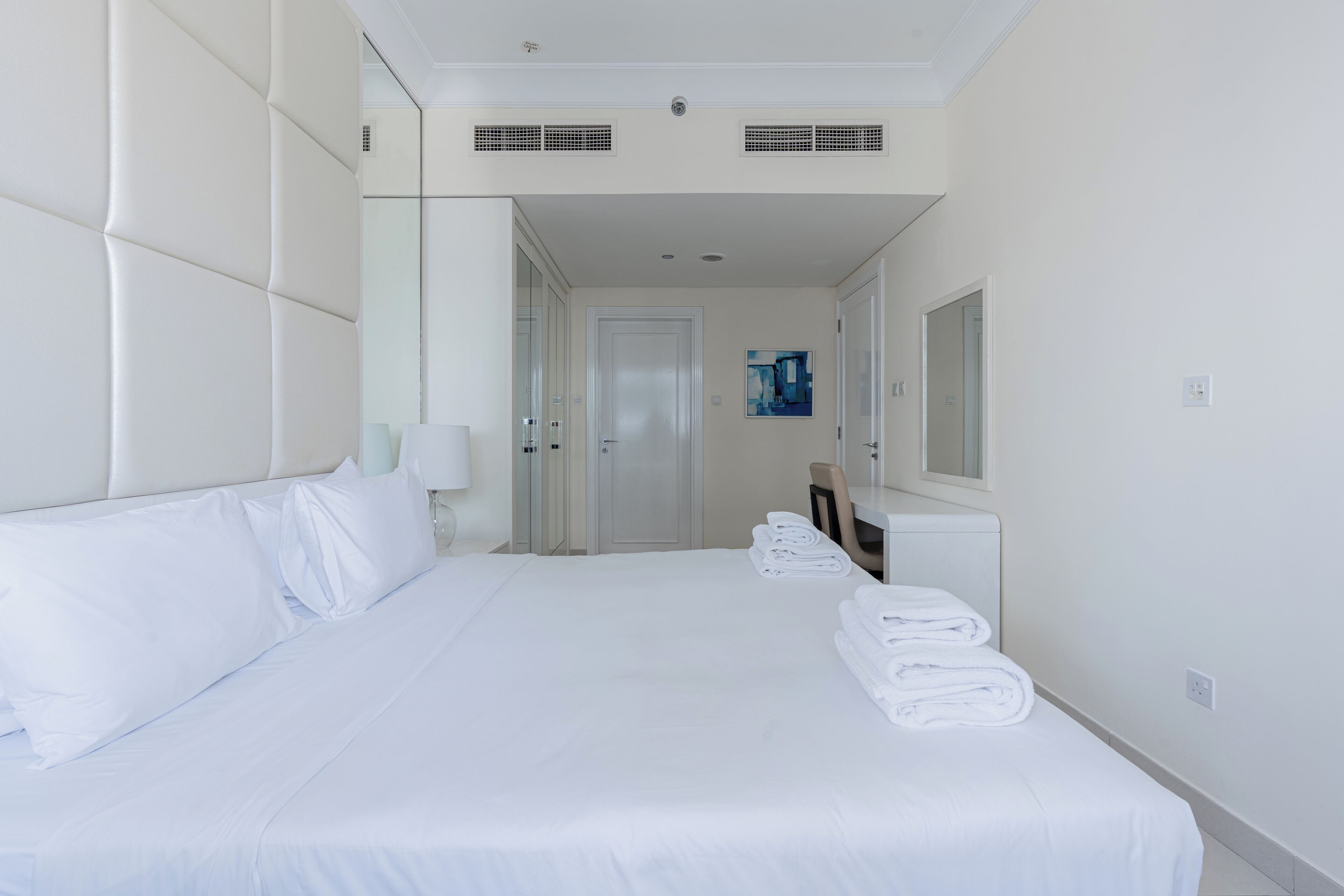 Habitación de hotel con una cama grande, un escritorio, una silla y un espejo.