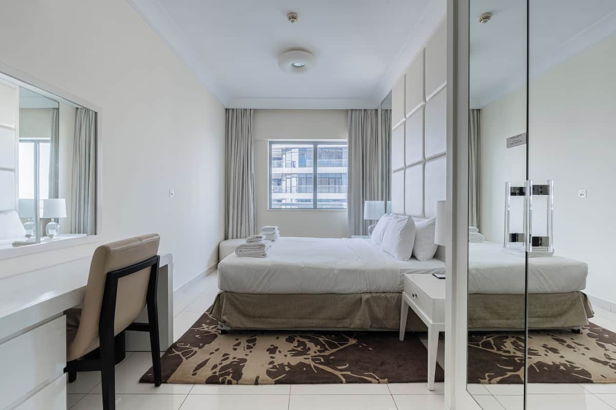 A hotel room with a bed, a desk, a chair, a large mirror, and a window with curtains.