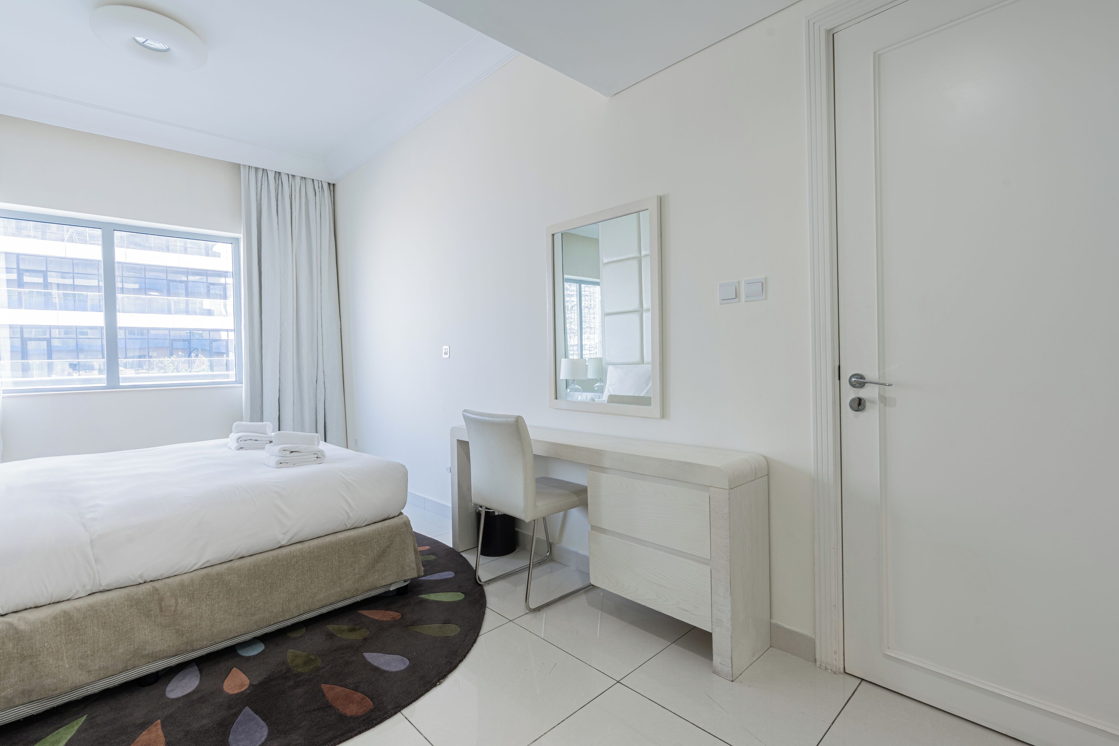 Habitación de hotel con cama, escritorio, silla, espejo y puerta.