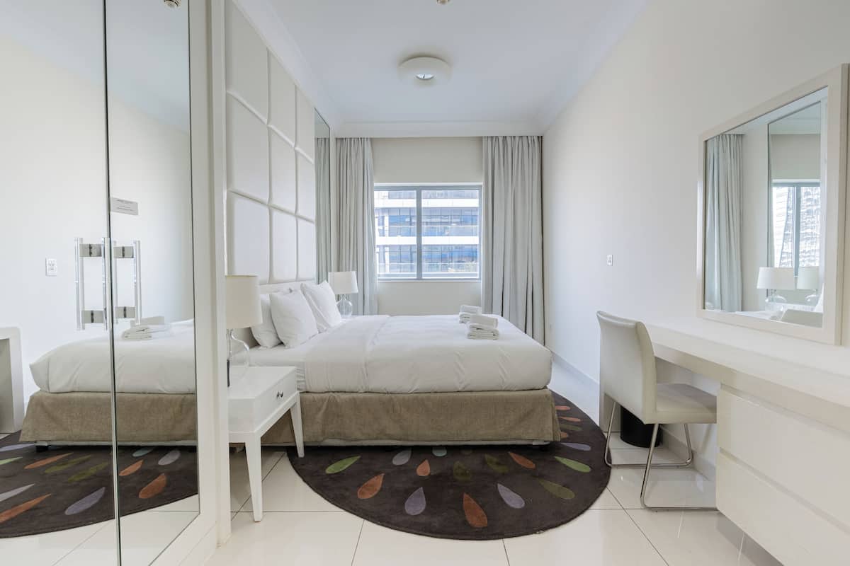A modern hotel room with a large bed, a desk, and a mirror.