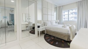 A modern hotel room with a large bed, a desk, a chair, and a view of the city through the window. - DAMAC Maison Mall Residences - Downtown (Dubai)