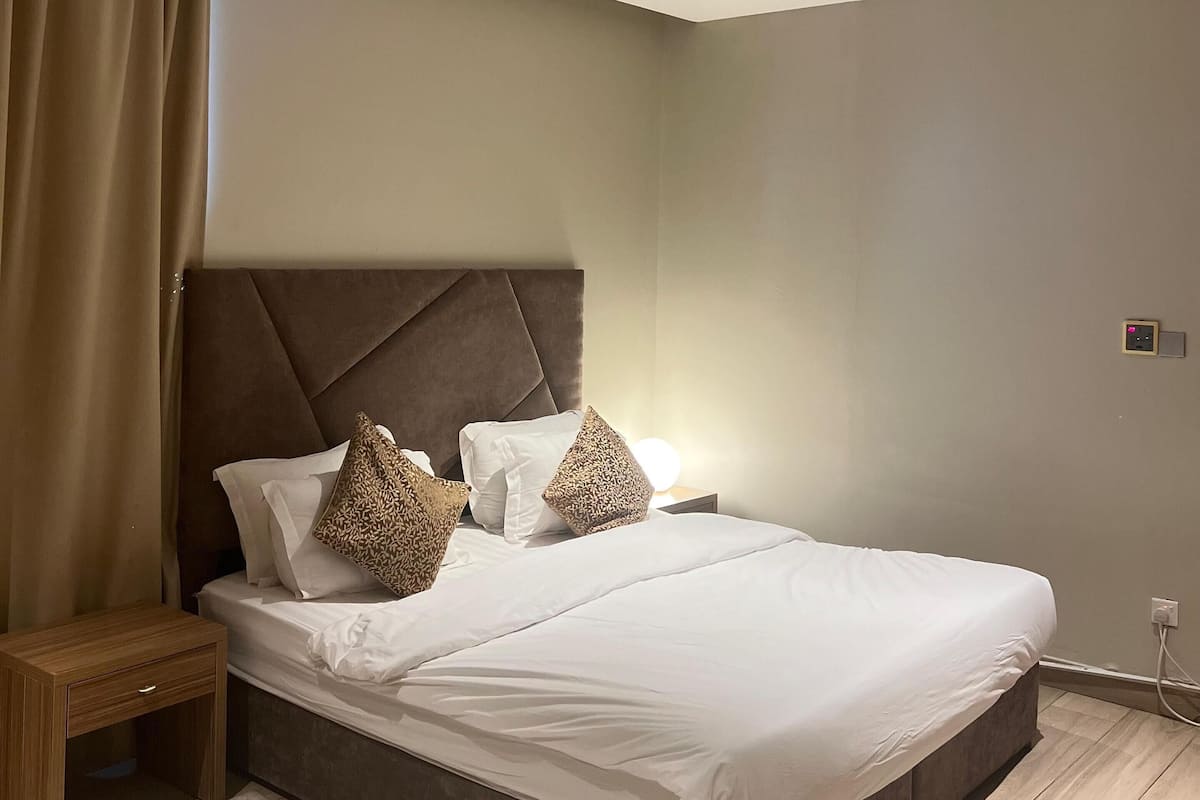 A modern bedroom with a large bed, a headboard, a bedside table, and a nightstand.