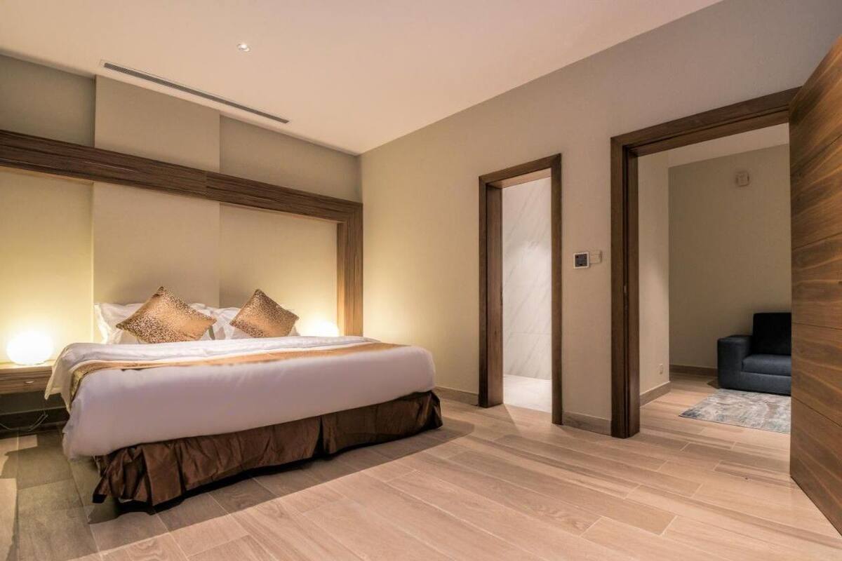 A modern hotel room with a large bed, wooden flooring, and a minimalist design.