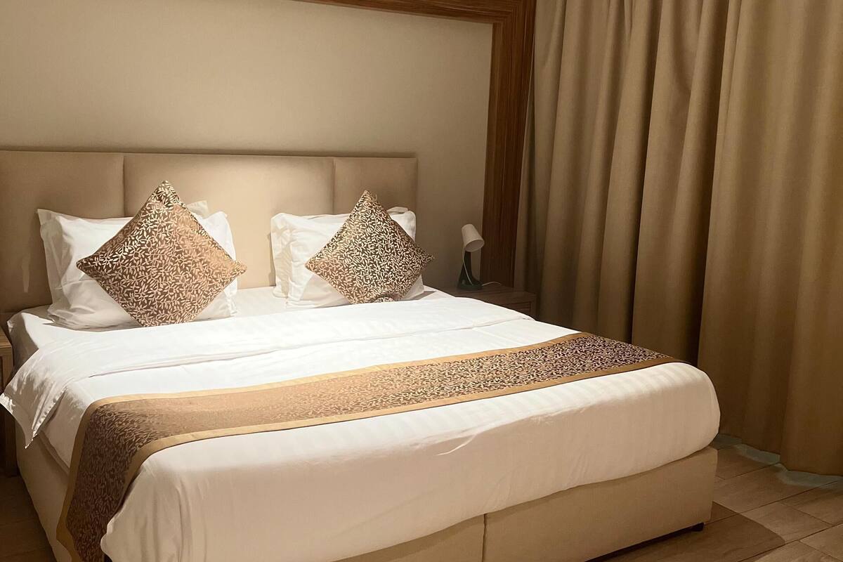 A large bed with a wooden headboard, two patterned pillows, and a beige bedspread.