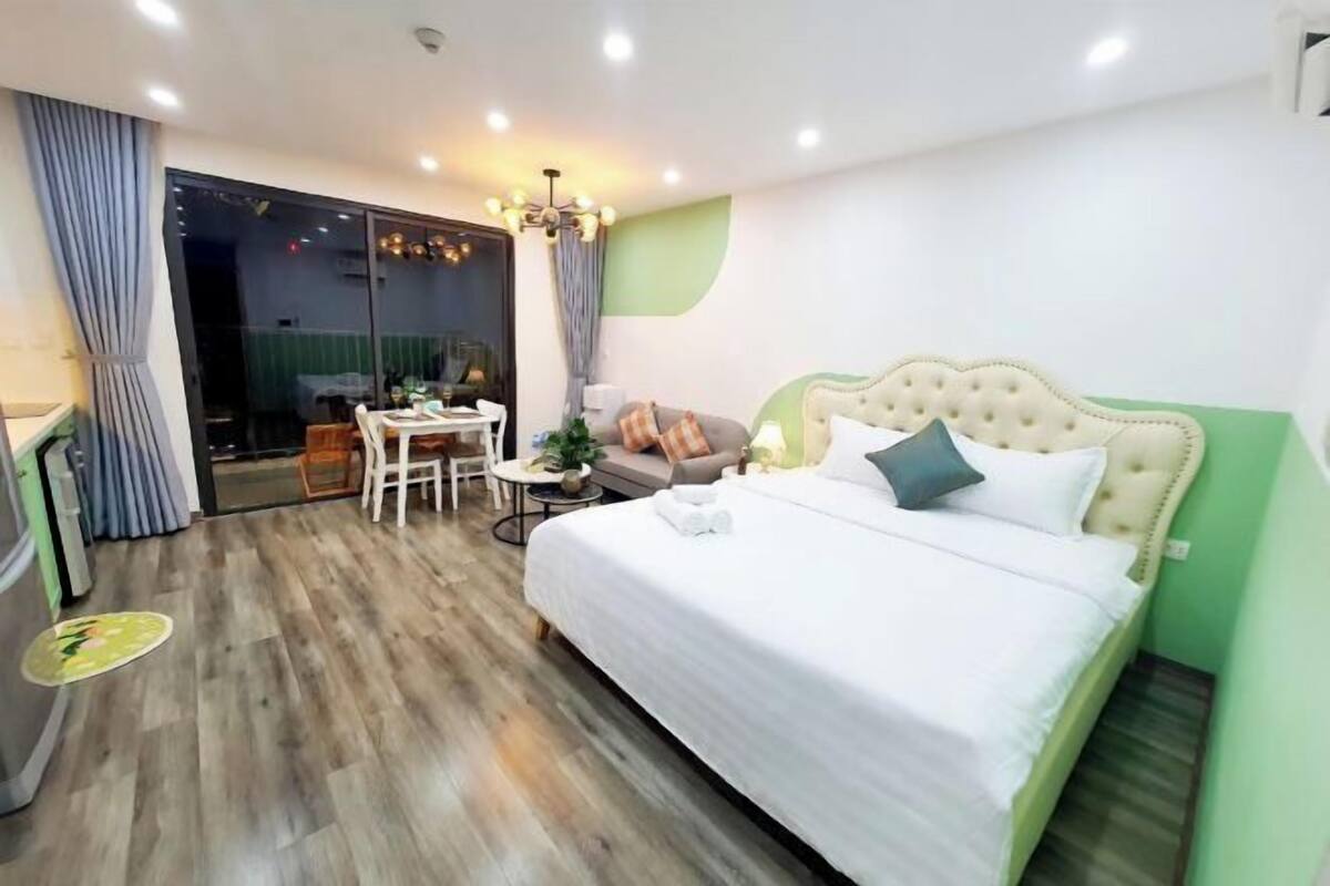 Habitació d'hotel amb llit, escriptori, cadira, taula petita, planta i una porta corredissa de vidre que dona a un balcó.