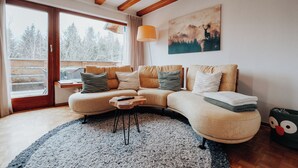 Ein gemütliches Wohnzimmer mit einem großen Ecksofa, einem Couchtisch und einem Gemälde von einer Berglandschaft.