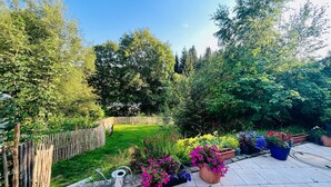 Ein Garten mit Holzzaun, einem Metall-Gießkann und verschiedenen Blumentöpfen.