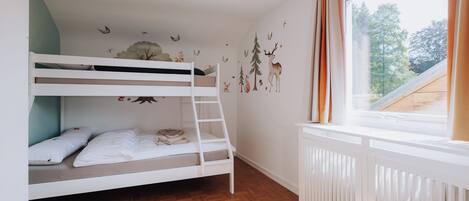 A bunk bed room with a wooden floor, a window with curtains, and wall decals of animals and trees.