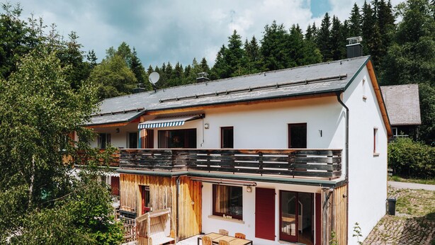 Ein zweistöckiges Haus mit Balkon, überdachter Sitzgelegenheit und Garten.