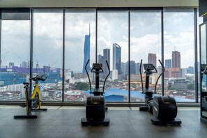 Une salle de sport équipée de matériel d’exercice et offrant une vue sur la ville grâce à de grandes fenêtres.