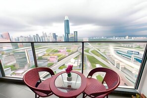 Ein Balkon mit Tisch und Stühlen, der auf einen Stadtblick mit einem markanten Wolkenkratzer und einer Autobahn blickt.