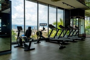 Ein Fitnessstudio mit Laufbändern und Trainingsgeräten, großen Fenstern und Blick auf eine Stadtansicht.
