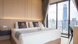 Ein modernes Hotelzimmer mit einem großen Bett, einem Nachttisch, einem Schreibtisch und Blick auf eine Stadtkulisse durch große Fenster.