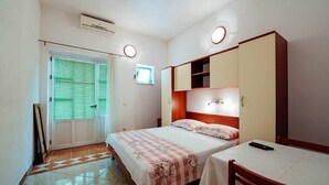 Une chambre à coucher comprenant un lit, une table de chevet, une chaise, une armoire et une fenêtre avec des stores.