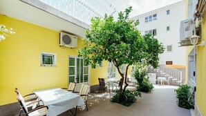 Une cour intérieure comprenant un espace repas, un arbre et un escalier menant à un niveau supérieur.