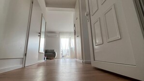 A hallway with white walls and wooden flooring leading to a room with a gray sofa and a window with sheer curtains. - Urban Luxury Apartment Zagreb  One  Bedroom Apartment (Zagreb)