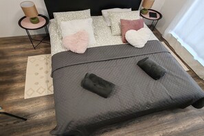 A neatly arranged bedroom with a bed, pillows, a bedside table with a lamp, and a small table with a book and a plant.