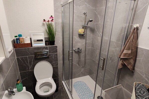 A modern bathroom with a glass-enclosed shower, a toilet, and a sink.