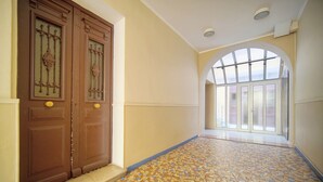 A hallway with patterned floor tiles, a large wooden door with a decorative glass panel, and a large arched window with frosted glass. - 2 Rooms with Balcony Hypercentre A1B162 (Cannes)