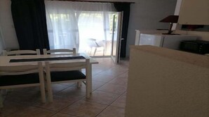 Zona pranzo con tavolo e sedie, angolo cottura con fornello e una porta scorrevole in vetro che dà su uno spazio esterno.
