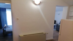 Ein Zimmer mit einem weißen Heizkörper, einem Bett mit blauer Vorhang und einem kleinen Tisch mit Lampe.