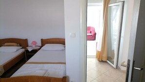 A hotel room with two single beds, a small table with a lamp, and a sliding glass door leading to a balcony with a pink chair. - Apartments Libertas - Two Bedroom Apartment with with Terrace and Sea View (7) (Rogoznica)