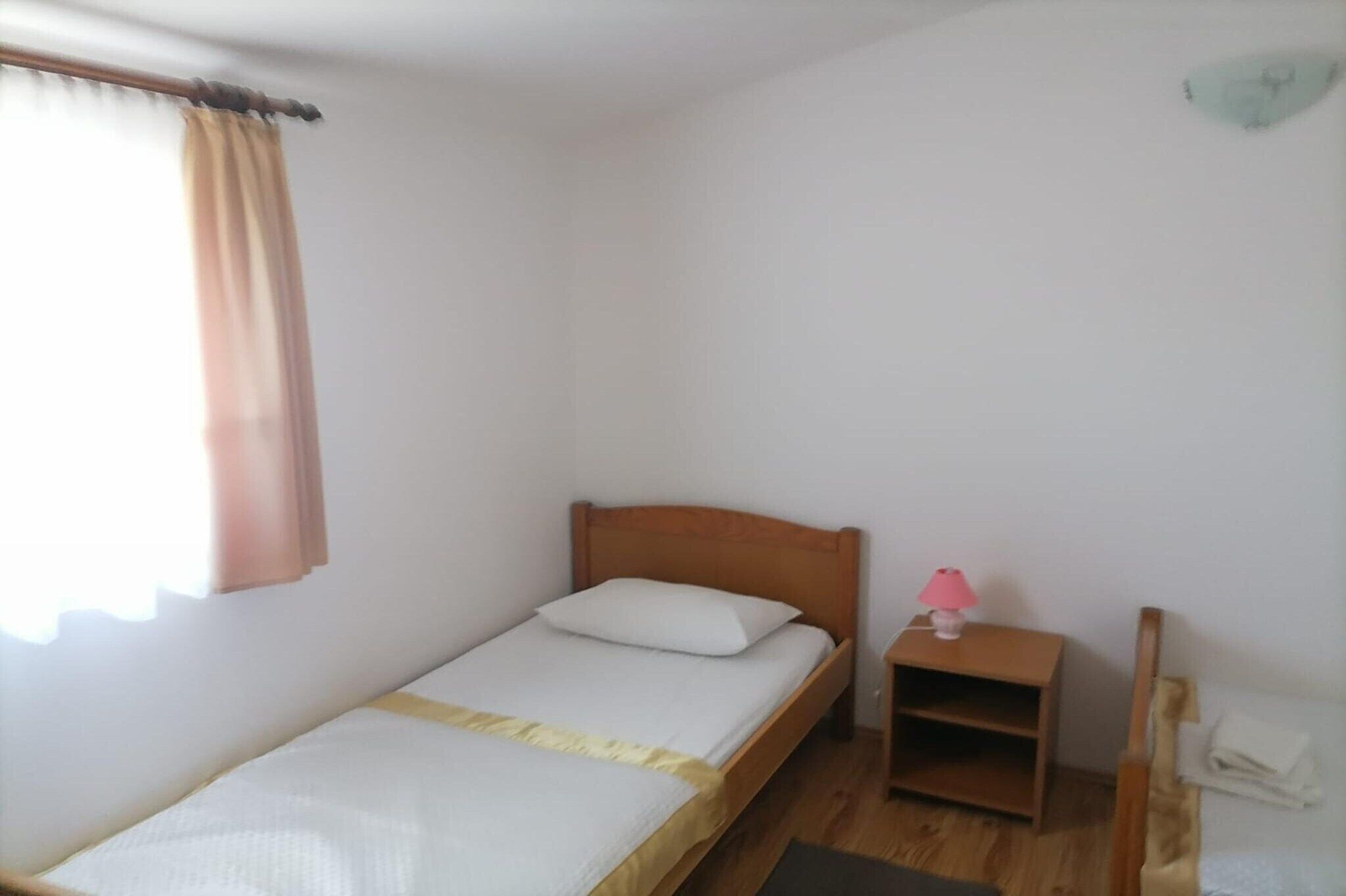 A single bed with a wooden headboard, a bedside table with a lamp, and a small shelf unit.