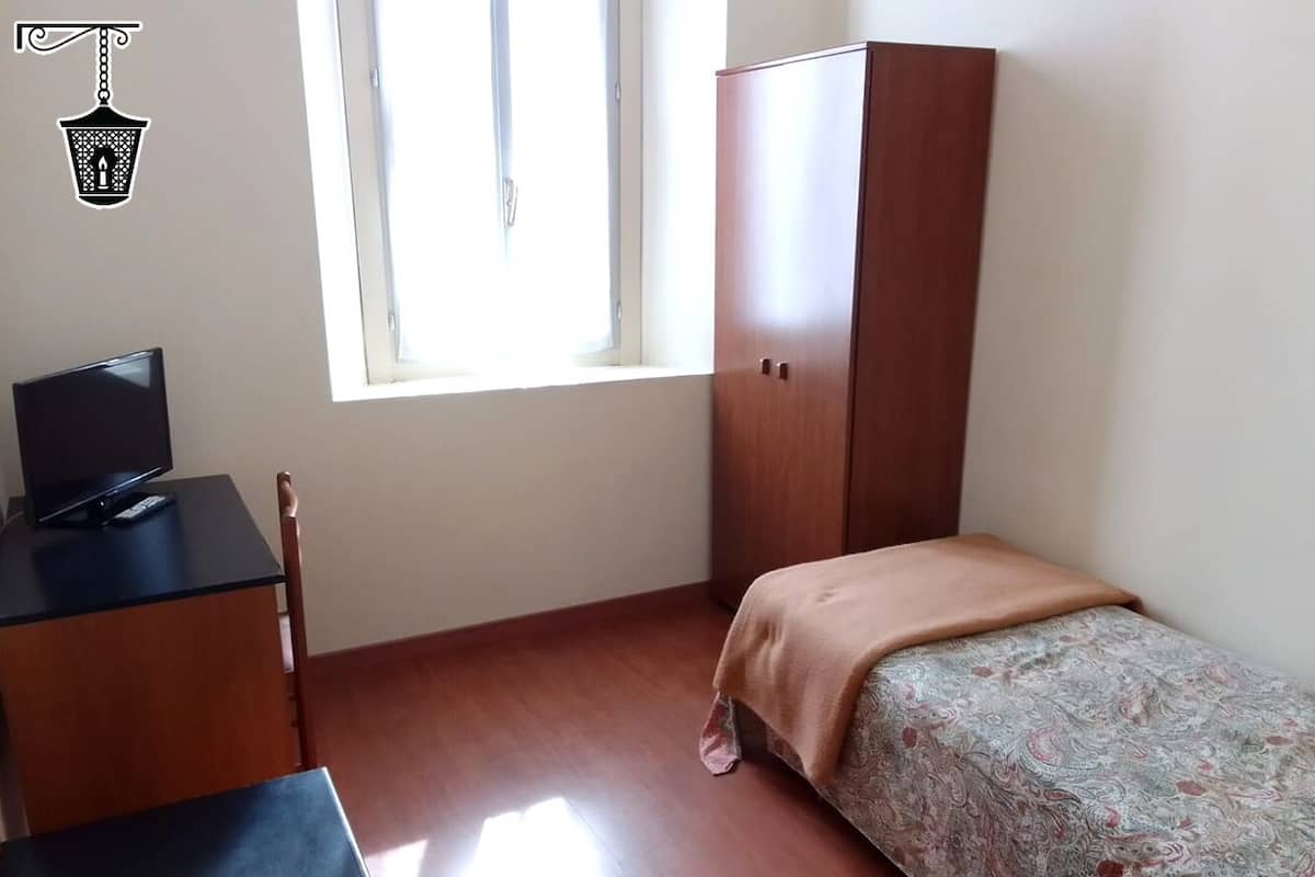 A small, well-lit room with a bed, a desk with a computer, and a wardrobe.