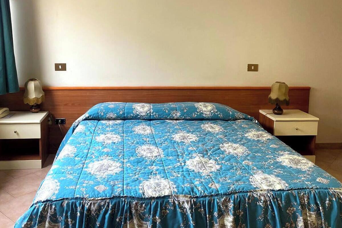 A bedroom with a bed, two bedside tables, a lamp on each, and a window with curtains.