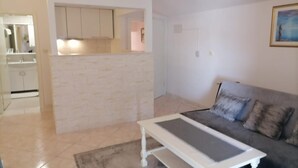 Una sala de estar con un sofá gris, una mesa de centro blanca y una cocina con gabinetes blancos y una pared de ladrillo decorativa.