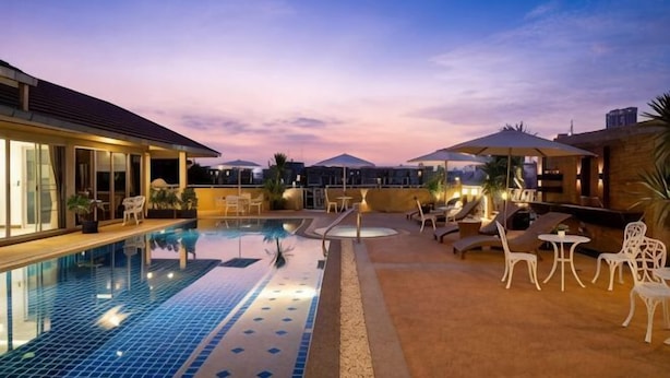 A swimming pool with lounge chairs and umbrellas, surrounded by a building with large windows.