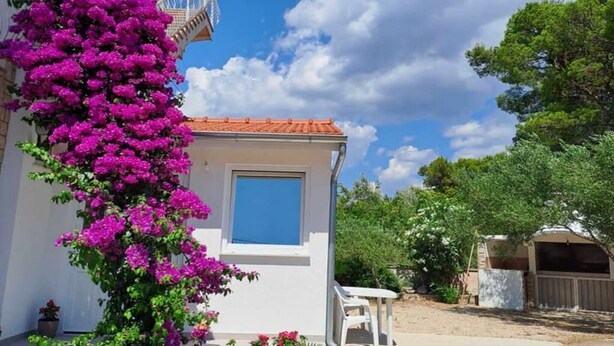 Un edificio blanco con techo de tejas rojas, una ventana pequeña y una silla blanca en el exterior.