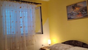Habitación de hotel con cama, mesita de noche, lámpara, un cuadro en la pared y ventana con cortinas.